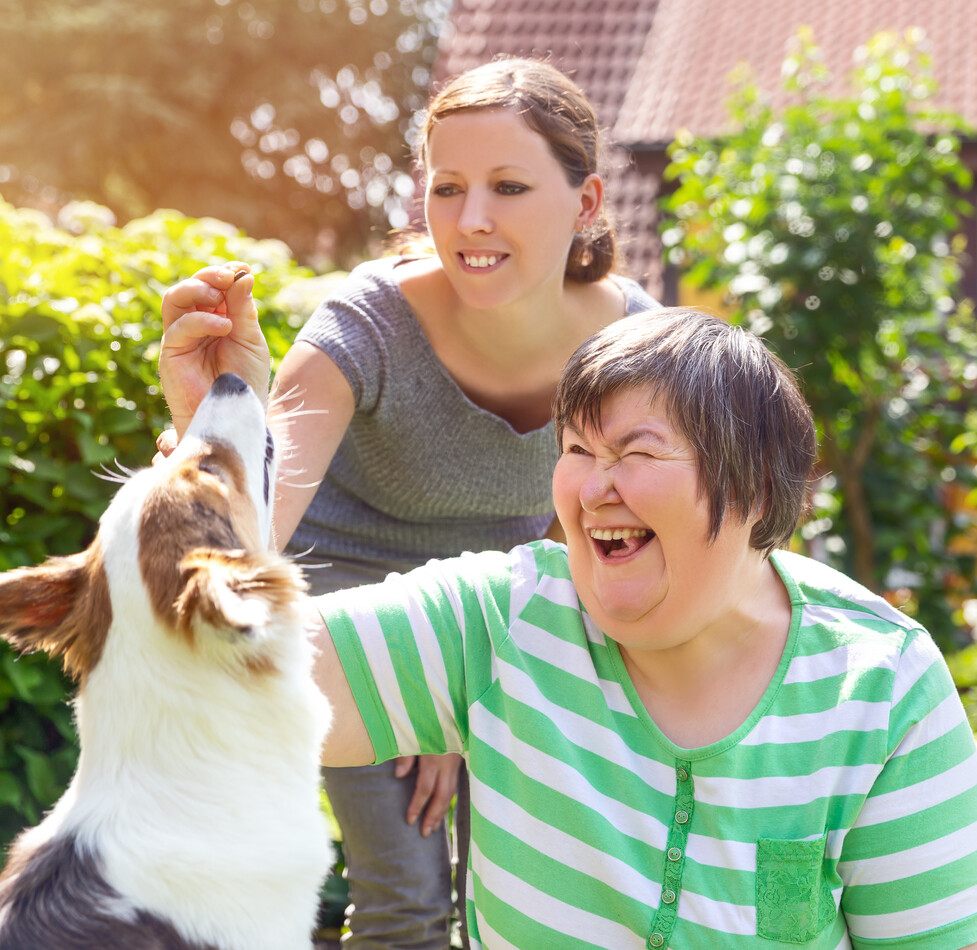 Tagesstrukturen für Menschen mit Behinderungen I Adobe Stock Zwei Frauen spielen mit einem Hund im Garten.