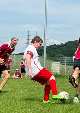 Drei Personen mit und ohne Behinderung spielen gemeinsam Fußball auf einer Wiese.