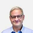Franz Ströbitzer Porträtaufnahme von Franz Ströbitzer, Standortleitung Maria Ponsee bei BALANCE. Er blickt mit einem herzlichen Lächeln direkt in die Kamera. Er hat kurzes, grau meliertes Haar und trägt eine dunkle, rundliche Brille sowie ein hellblaues Hemd vor einem neutralen, hellen Hintergrund.