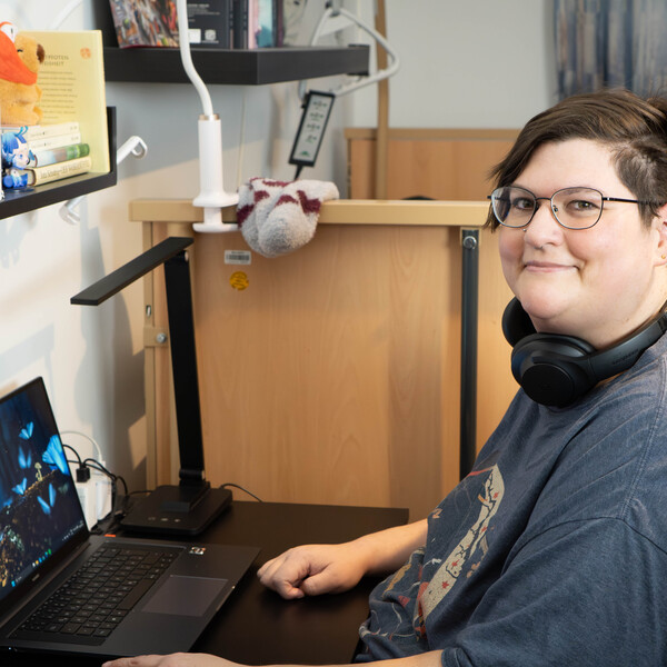 Bewohnerin Claudia sitzt in ihrem Zimmer vor ihrem Laptop und lächelt in die Kamera