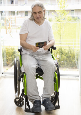 Ein Mann sitzt im Rollstuhl und hält ein Buch in der Hand.