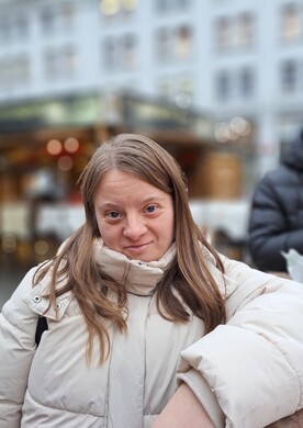 Eine junge Frau mit Behinderung und langen braunen Haaren blickt selbstbewusst in die Kamera.