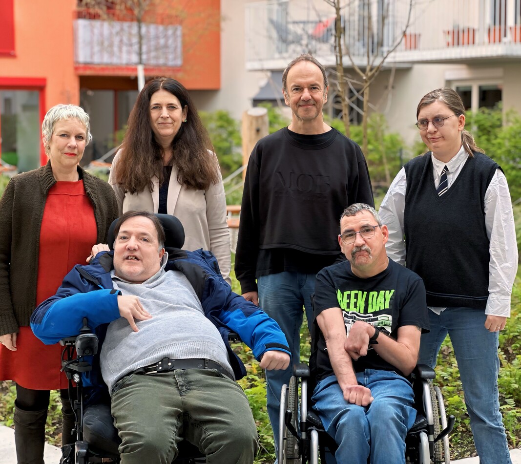 Inklusive Redaktion (c) Oliferenko Sechs Personen aus dem Team der inklusiven Redaktion des Magazins Balancer sitzen und stehen gemeinsam in einem begrünten Innenhof.