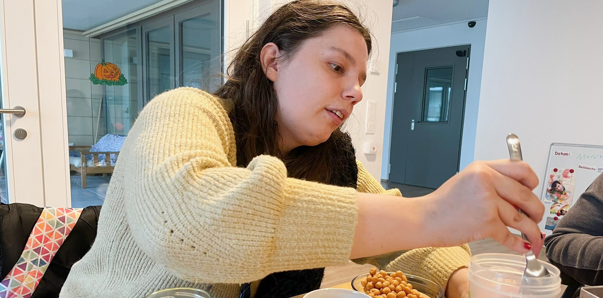 WVB Hermann Glück I BALANCE Frau bereitet an einem Tisch Essen vor und füllt Kichererbsen in einen Behälter – eine Alltagssituation beim selbstständigen Wohnen.