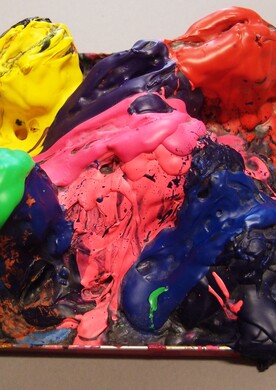 Ein dreidimensionales, plastisches Kunstwerk der Künstlerin Andrea Meija Rocha. Es handelt sich um eine rechteckige Palette, auf der sich dicke Schichten von Acrylfarbe zu hohen, reliefartigen Hügeln aufgetürmt haben. Die Oberfläche ist glänzend und zeigt kräftige Farben wie leuchtendes Gelb, sattes Rot, knalliges Pink und sattes Grün, die über eine dunkle, fast schwarze Basis aus eingetrockneter Farbe fließen. Die Struktur wirkt organisch und erinnert an erkaltete, bunte Lava.