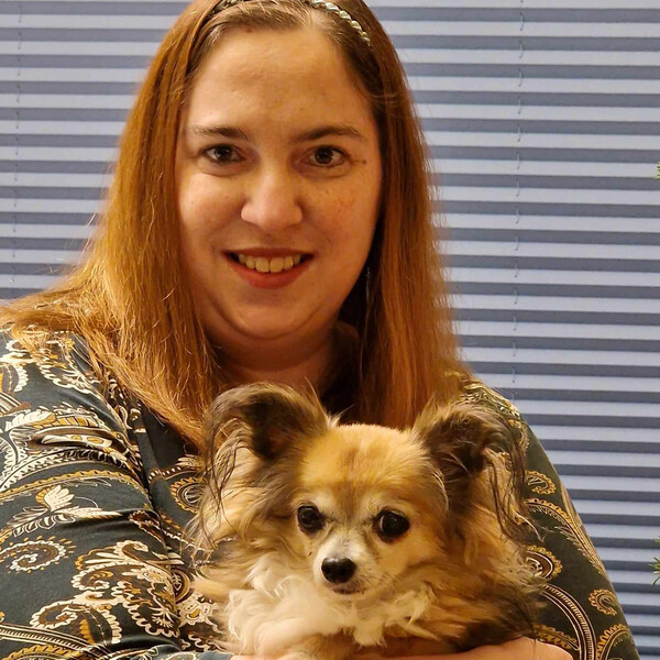 WVB Hermann Glück I BALANCE Bewohnerin Michelle lächelt in die Kamera. Sie hat lange hellbraune Haare und einen kleinen Hund im Arm.