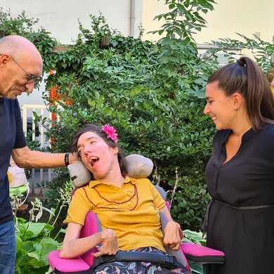 Bei einem Gartenfest stehen und sitzen vier Personen mit und ohne Behinderung nebeneinander und unterhalten sich.