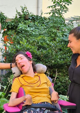 Bei einem Gartenfest stehen und sitzen vier Personen mit und ohne Behinderung nebeneinander und unterhalten sich.